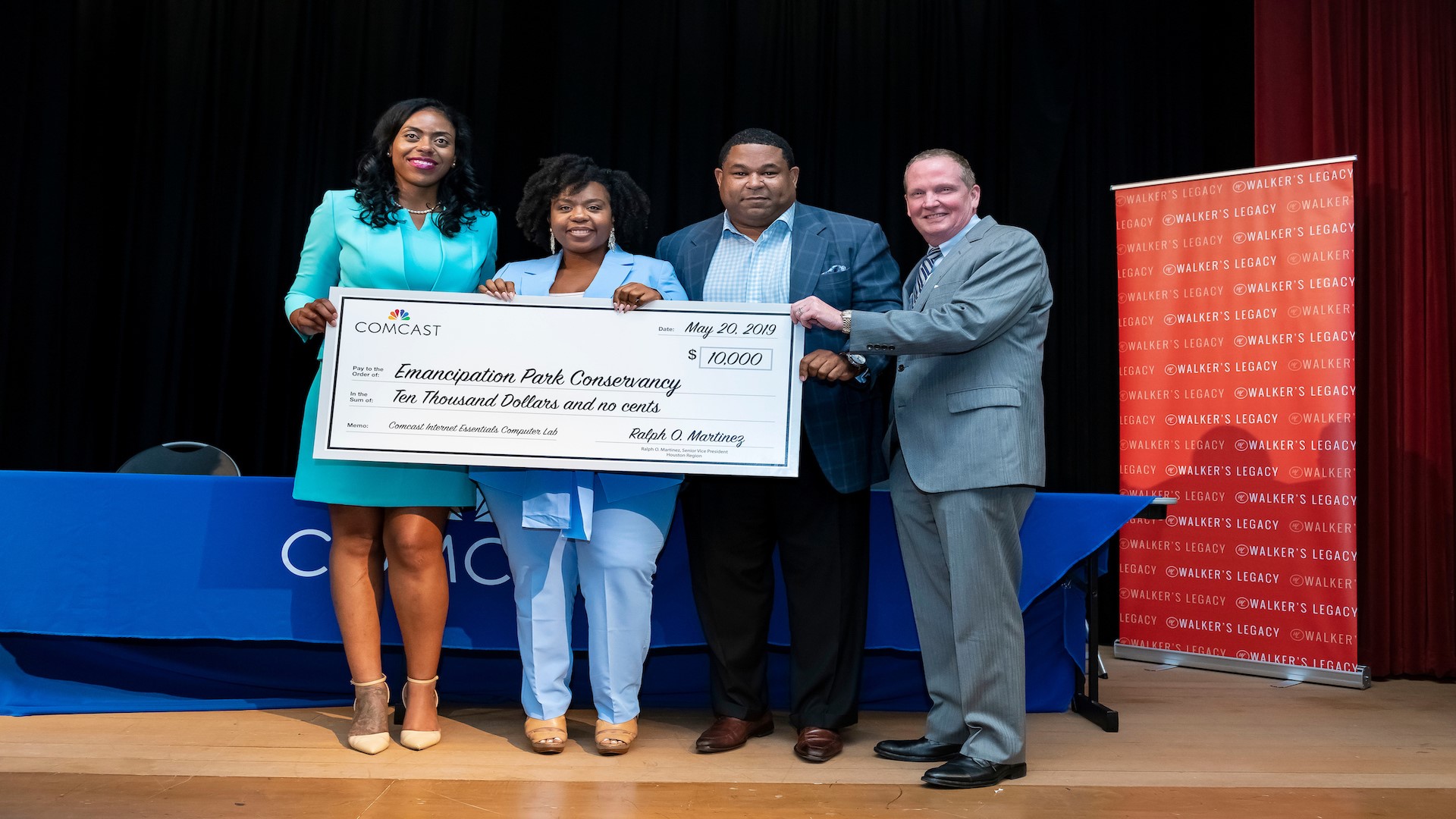 Four people onstage at the Women of Color in Tech event hold an oversized check made out to the Emancipation Park Conservancy